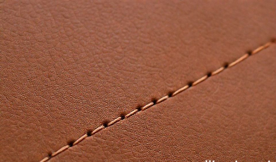 A person's hands carefully saddle-stitching a leather journal, with traditional tools laid out on a worn workbench.